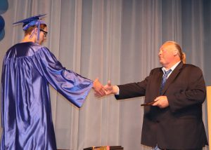 a young man wearing a cap and gown shakes the hand of a teacher on a stage