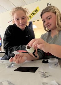 two young female students use tape to extract fingerprints from a mock crime scene