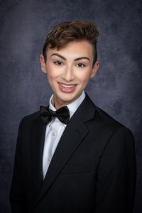 a young man wearing a tuxedo poses in front of a backdrop