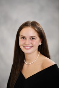 a girl with long dark straight hair wearing a pearl necklace poses for a senior portrait