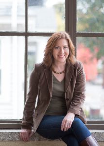 a woman wearing a brown jacket sits on a window sill