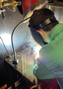 a young man wearing a green shirt and protective headgear is welding