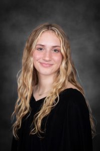a young woman with blonde wavy hair wears a black off the shoulder outfit for a posed photo
