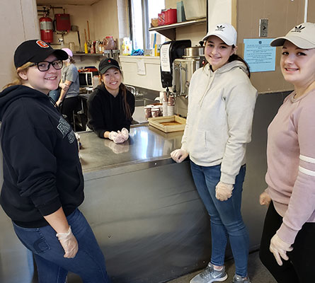 NHS member students stand by kitchen serving window