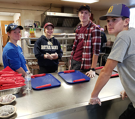 NHS member students stand by kitchen serving window