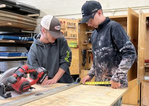 two young men measure something on a work table