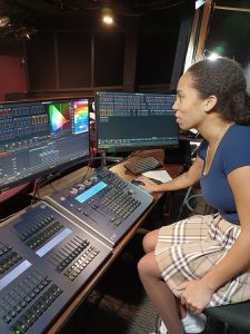 a young woman wearing a skirt sits in a chair behind an audio board