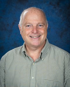 a man wearing a button down shirt poses in front of a blue background