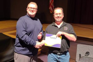 a teenaged boy shakes the hand of a man who is holding a certificate