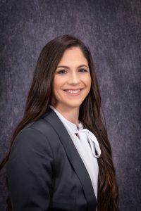 a woman with long dark hair wears a grey blazer with a white shirt underneath