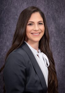 a woman with long dark hair wears a grey blazer with a white shirt underneath