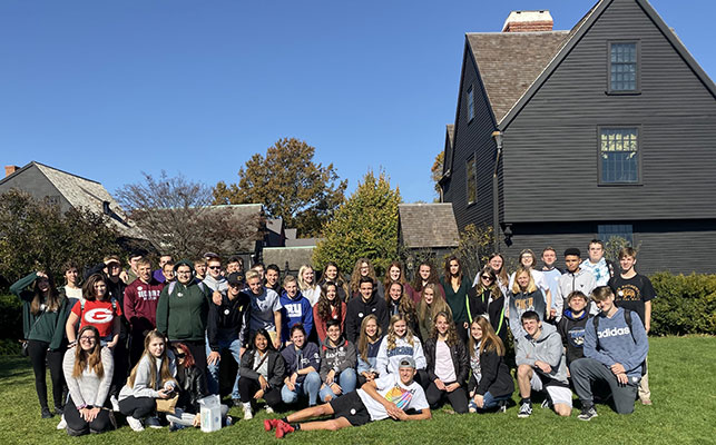 Group of students standing and sitting in front of the House of Seven Gables