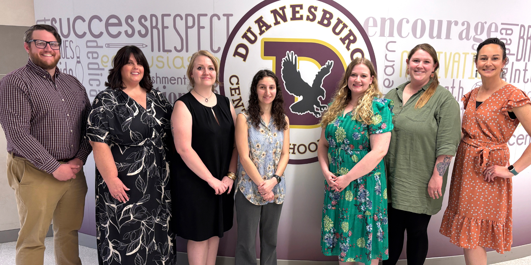 a group of young educators pose in a hallway in front of a school logo