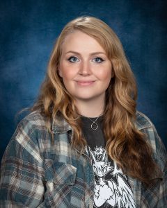 a woman with long blonde hair wears a t-shirt and a flannel shirt