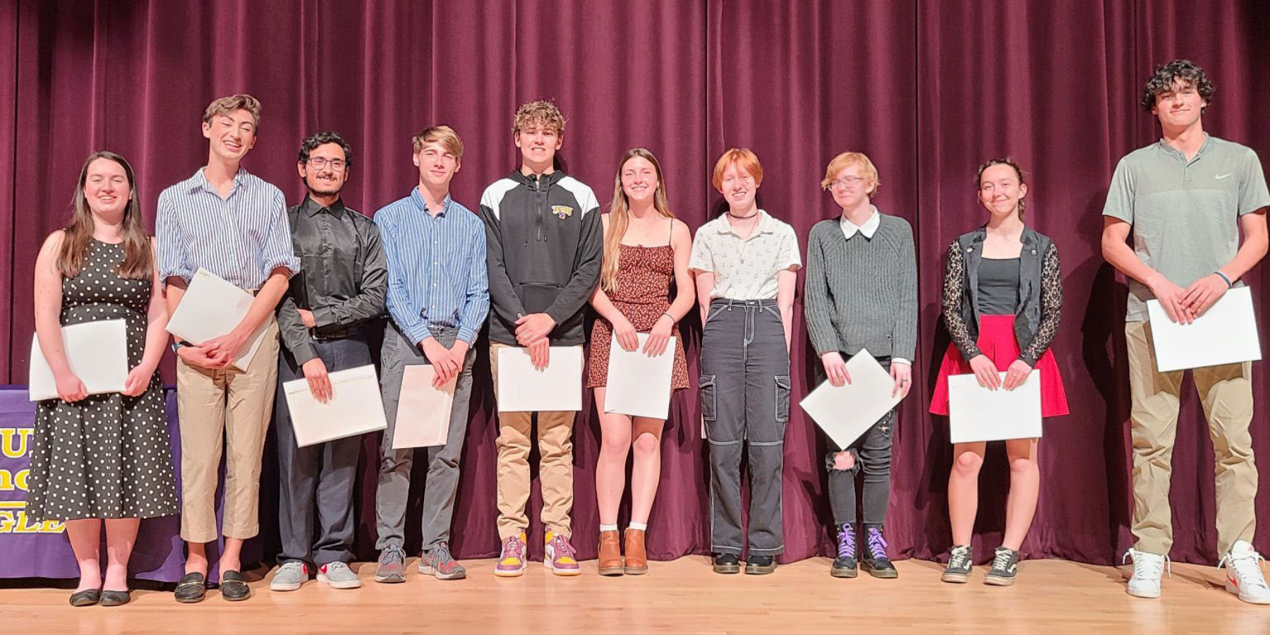 ten high school students stand on a stage holding certificates