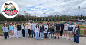 a group of teenagers pose in front of a baseball field