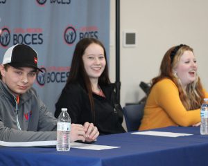 three teenage students sit at a table covered by a blue tablecloth