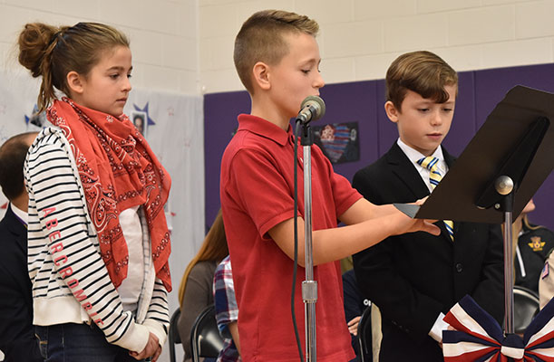 boy speaking into microphone, girl and another boy standing by his side