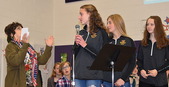 women holding check with hands up while high school girl students look on