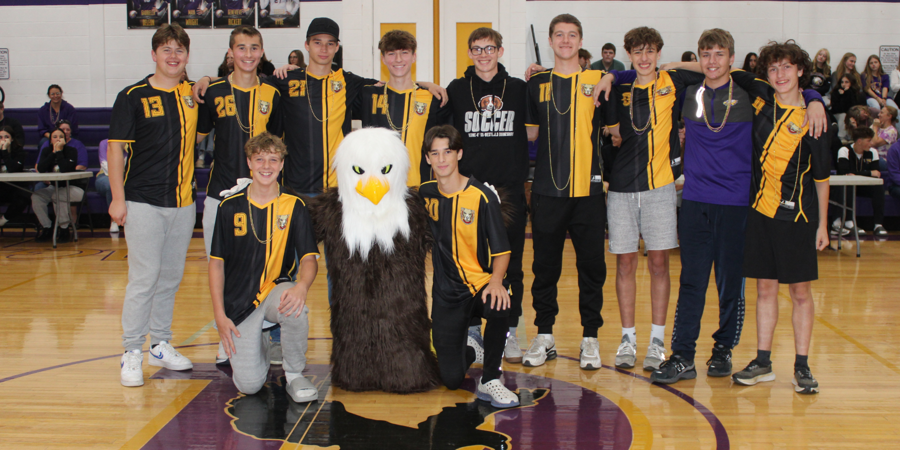 a group of teen male athletes pose in a gymnasium with an eagle mascot