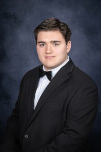 a young man with dark hair off to the side wears a suit and bowtie for a posed photo