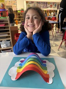 a girl poses with a rainbow that she created with construction paper