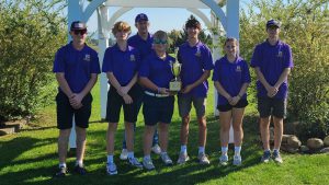 a golf team wearing purple shirts poses outside holding a trophy