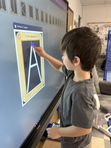 a child traces the letter "A" on a smart board