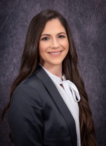 a woman with dark hair wearing a grey suit and white shirt smiles