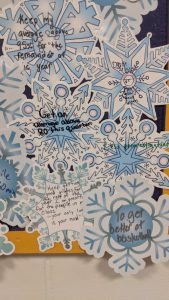 a close-up view of a collage on a bulletin board showing paper cutouts of snowflakes on blue and white paper showing handwritten notes from students sharing what their goals are