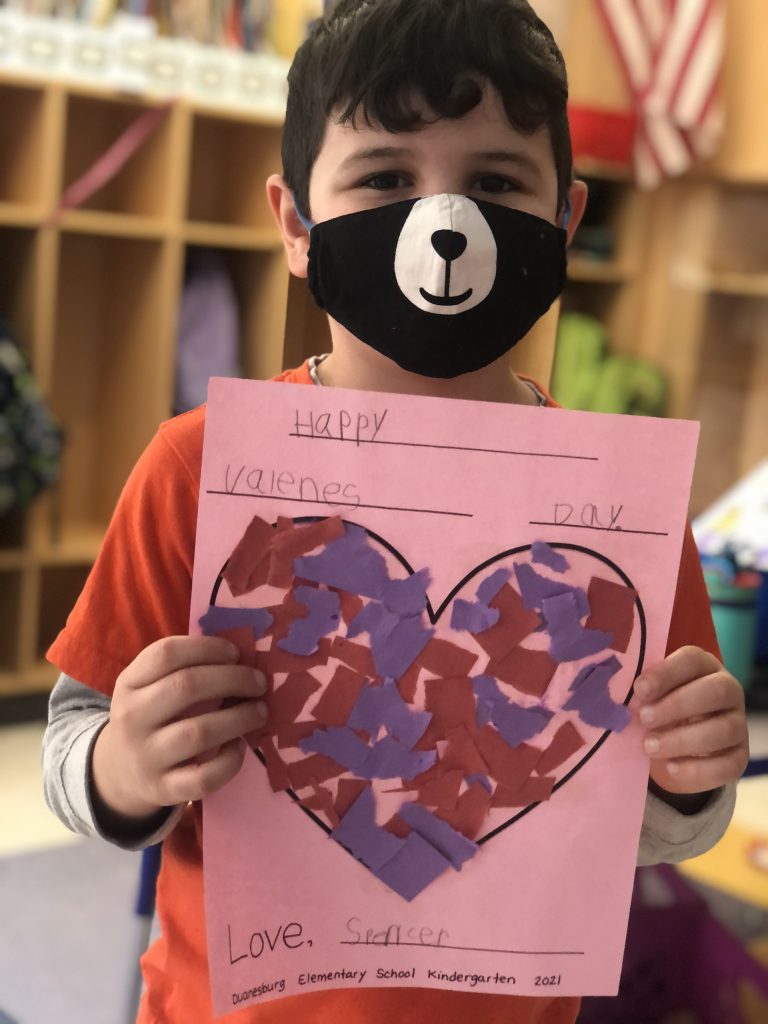 student wearing a mask with a bear face holds a handmade valentine