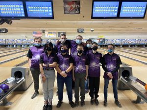 a team of nine bowlers wearing purple jerseys and face masks pose at the bowling alley