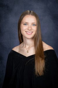 a young woman with long brown hair wears a black off the shoulder outfit for a posed photo