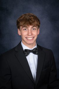 a young man with brown hair wears a suit and bowtie for a posed photo