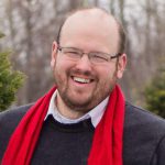 portrait of a person with short hair, glasses, and a beard while wearing a red scarf