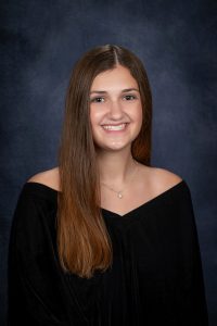 a young woman with brown hair wears a black off the shoulder outfit for a posed photo
