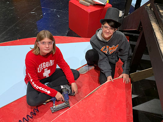 a female and a male student working with staple gun on set on stage