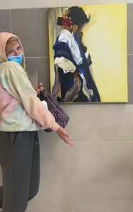 a young female student poses along side a portrait that she created.